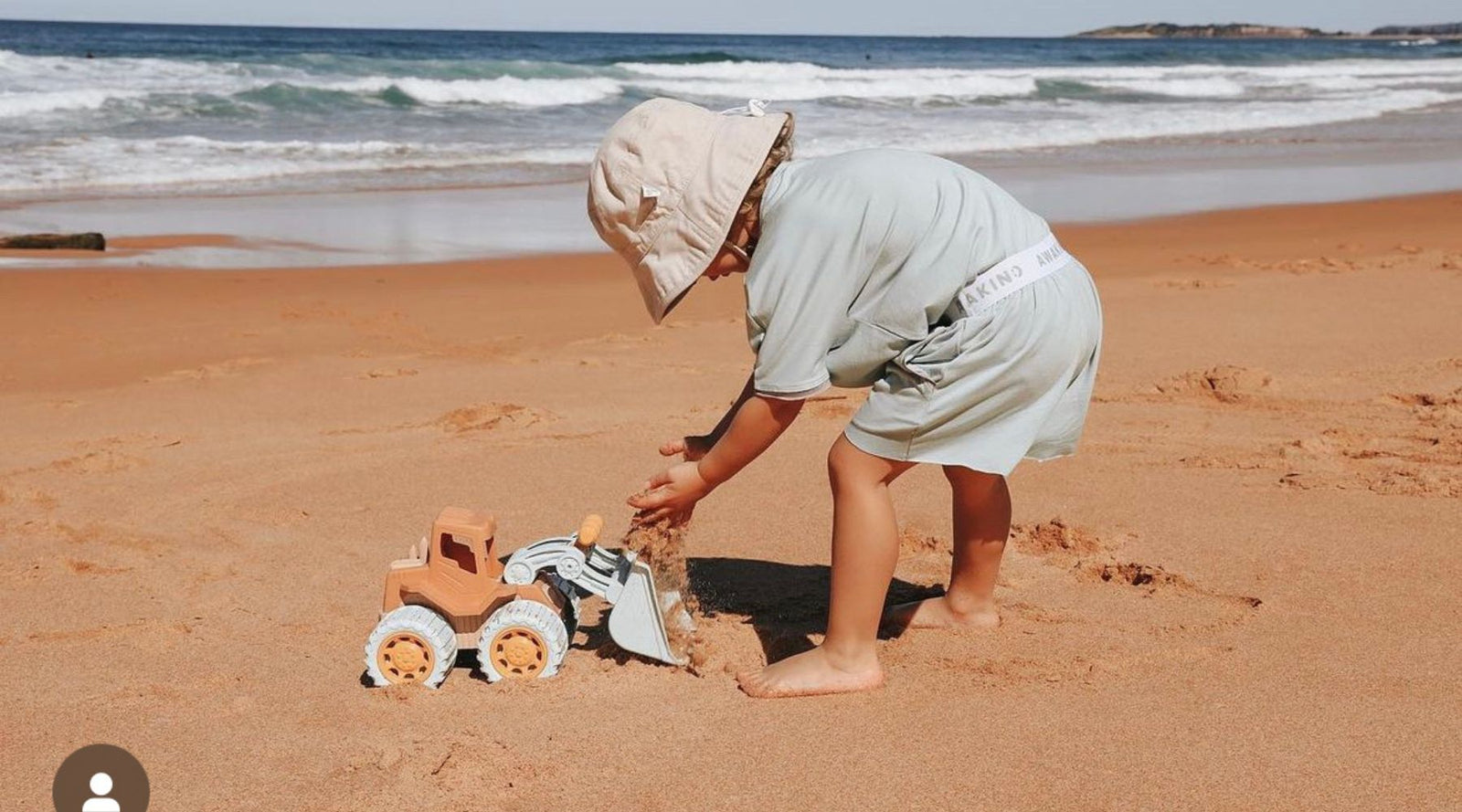 Picture of a child on the beach wearing a light green bamboo t-shirt and shorts, playing with a kids truck in the sand